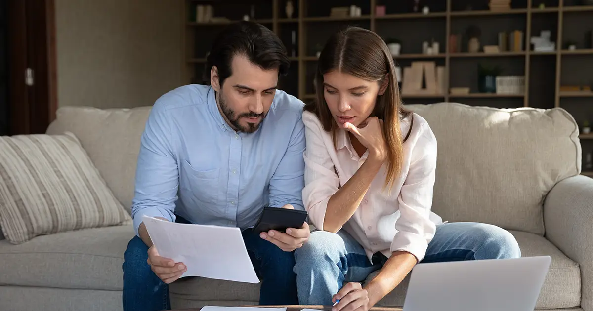 Un mari et une femme concentrés sont assis à table à la maison et examinent la paperasse.