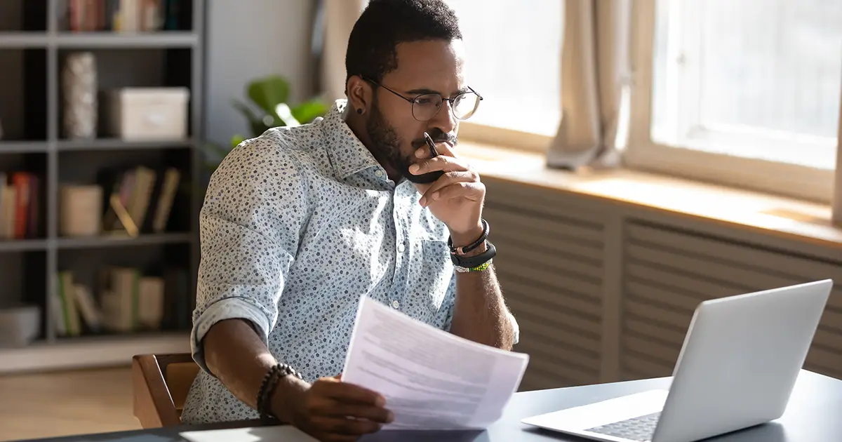 Homme concentré tenant des documents regardant l'écran d'un ordinateur portable