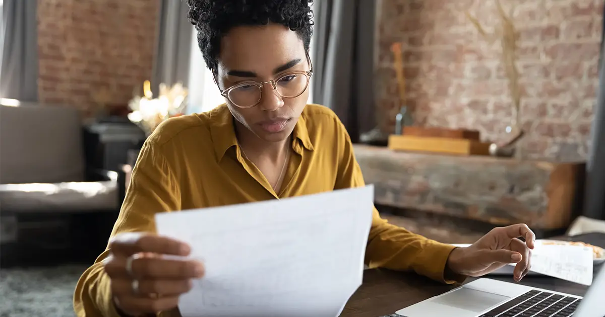 Jeune femme concentrée portant des lunettes, regardant des documents papier gérant des affaires commerciales
