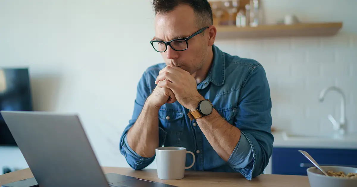 homme perdu dans ses pensées devant un ordinateur portable réfléchissant à la solution d'un problème