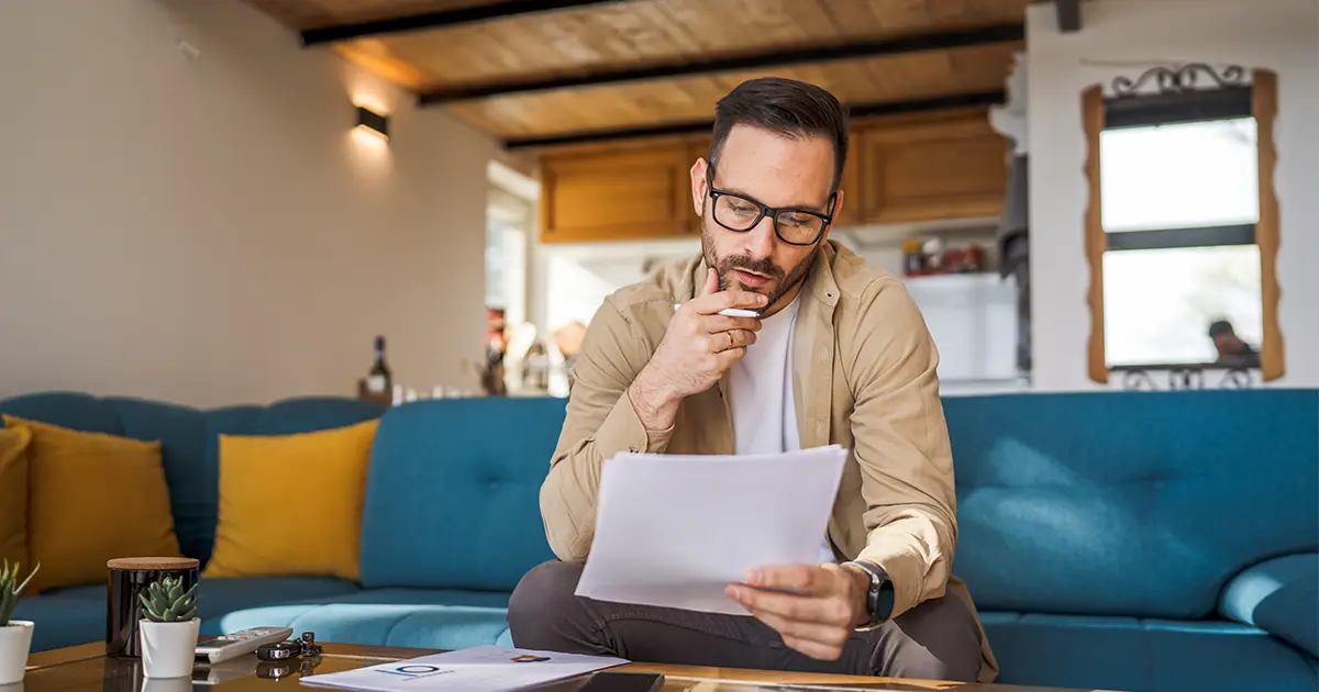 Un homme assis sur le canapé travaillant à la maison en tenant des documents en papier.