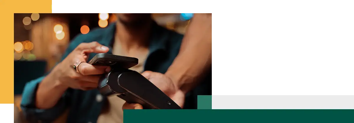 Gros plan sur un client payant avec son cellulaire et un terminal de paiement.