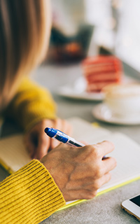 Une femme écrit en réfléchissant à la rédaction d'un budget dans un bloc-notes