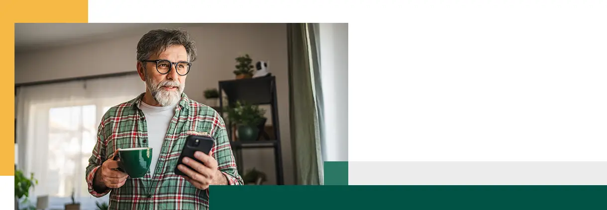 Un homme mûr barbu s'amuse en utilisant son téléphone portable et en buvant du café.