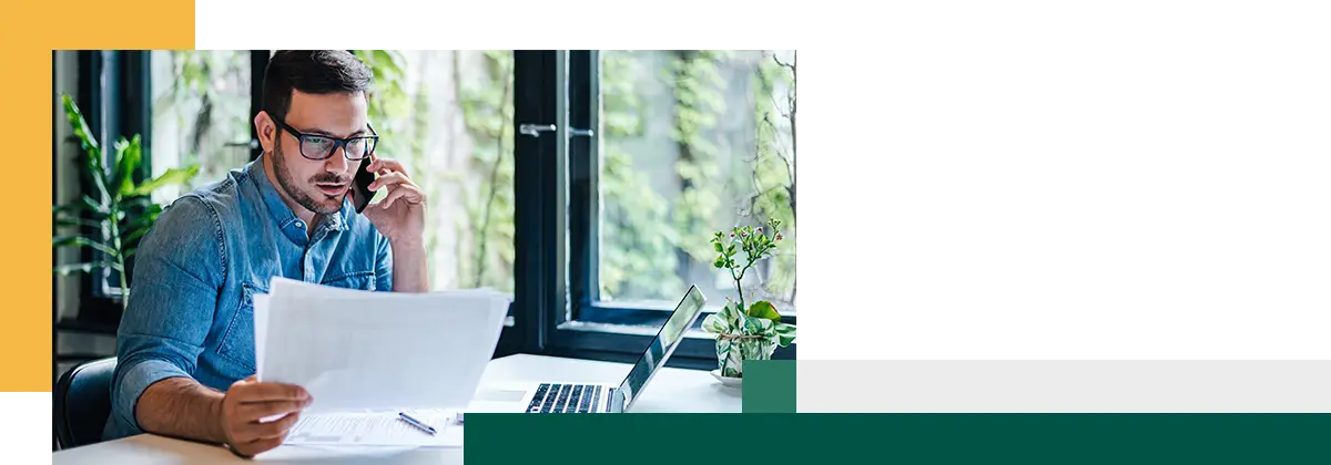Portrait d'un jeune homme travaillant à distance, tenant une feuille de papier et lisant un document financier.