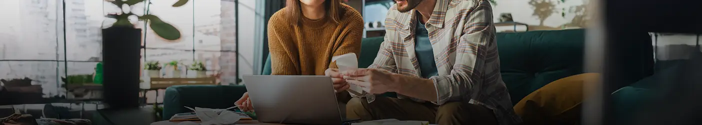 Un couple utilise un ordinateur portable assis sur un divan dans un appartement.
