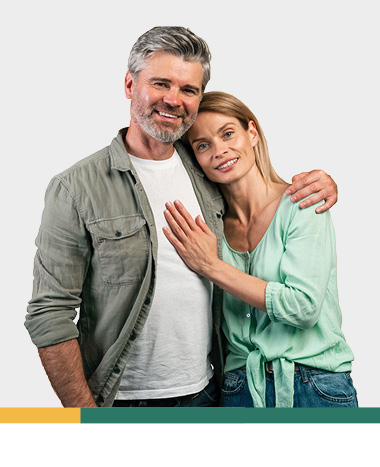 Couple d’adultes souriants debout ensemble, une personne posant la tête sur l’épaule de l’autre, vêtements décontractés sur fond clair.