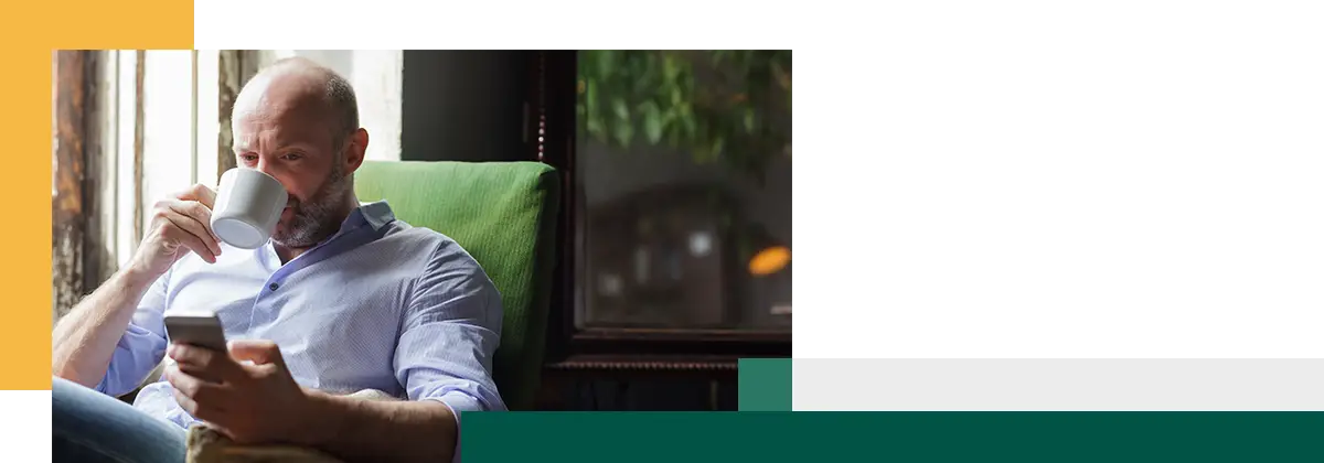 Un homme boit du café et consulte les actualités sur son téléphone.