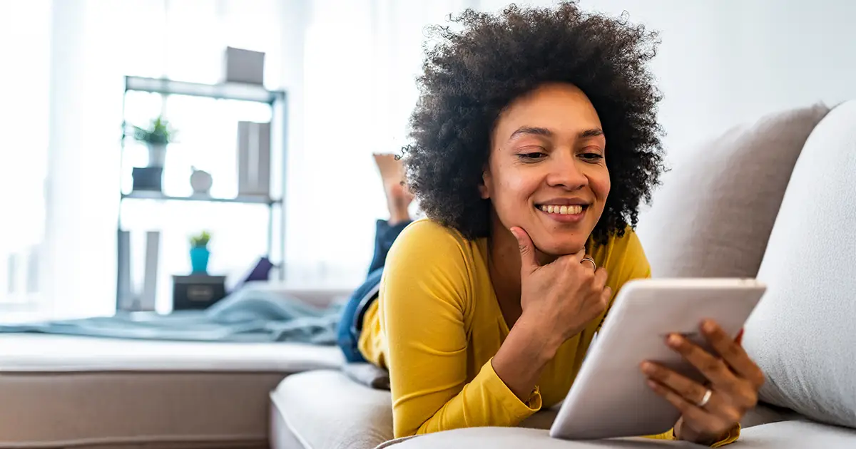 Heureuse jeune femme avec une tablette d'ordinateur allongée sur un divan