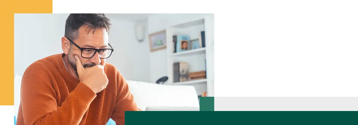 Un homme adulte pensif devant un ordinateur portable ouvert réfléchissant